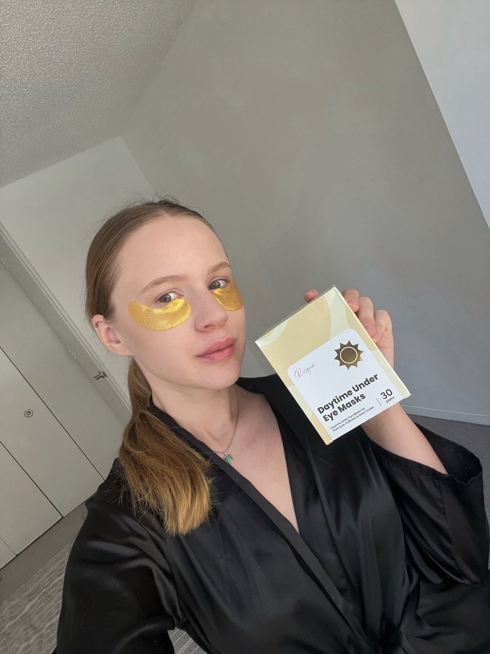 Anastasiia wearing gold eye masks and holding the product box